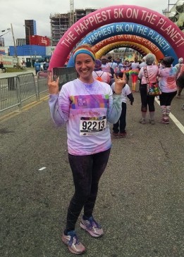 Morgan after a 5k, covered in colored dust, with both hands held up throwing horns