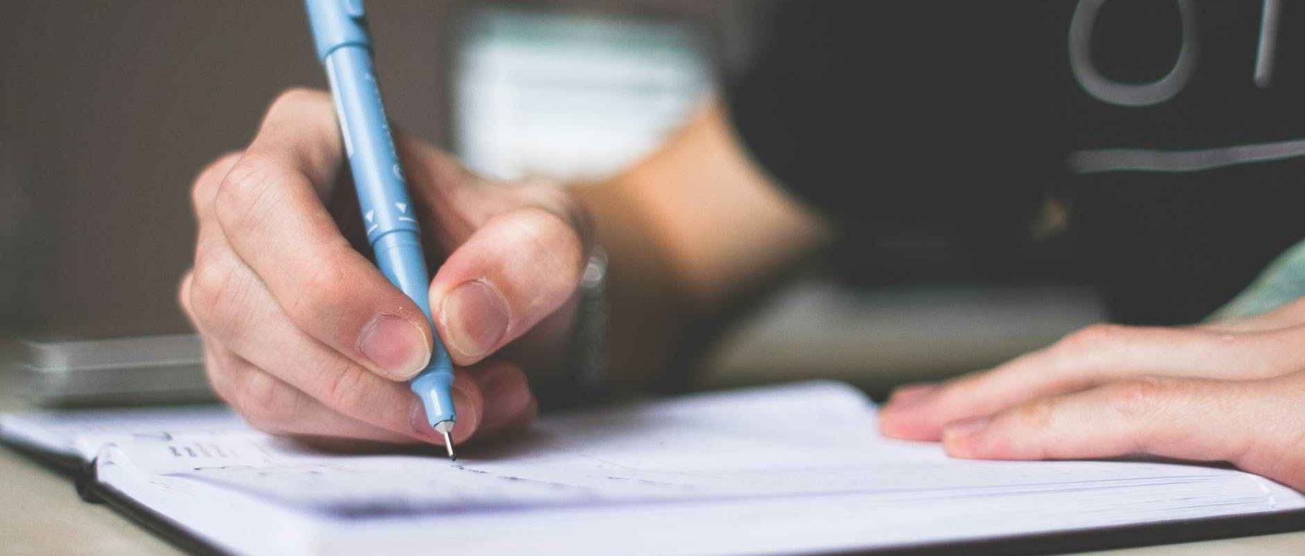 Person holding a blue ballpoint pen writing.