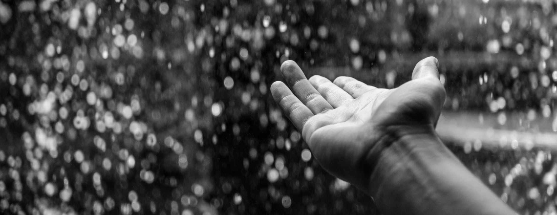 A hand reaching out to feel the falling rain - in black and white/greyscale.