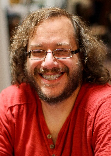 Keith DeCandido's profile picture. He's a white male with wavy shoulder-length brown hair, with a neatly trimmed beard and moustache, wearing a red shirt and rectangular glasses.